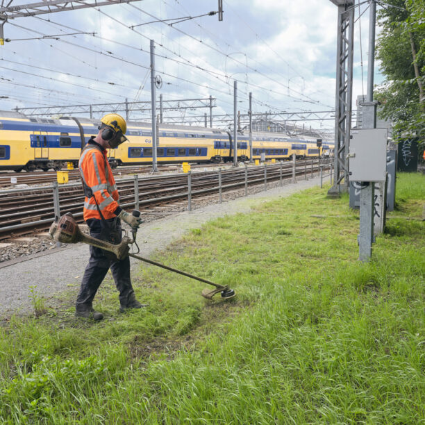 Met de bosmaaier aan het werk langs het spoor bij Amsterdam Centraal.